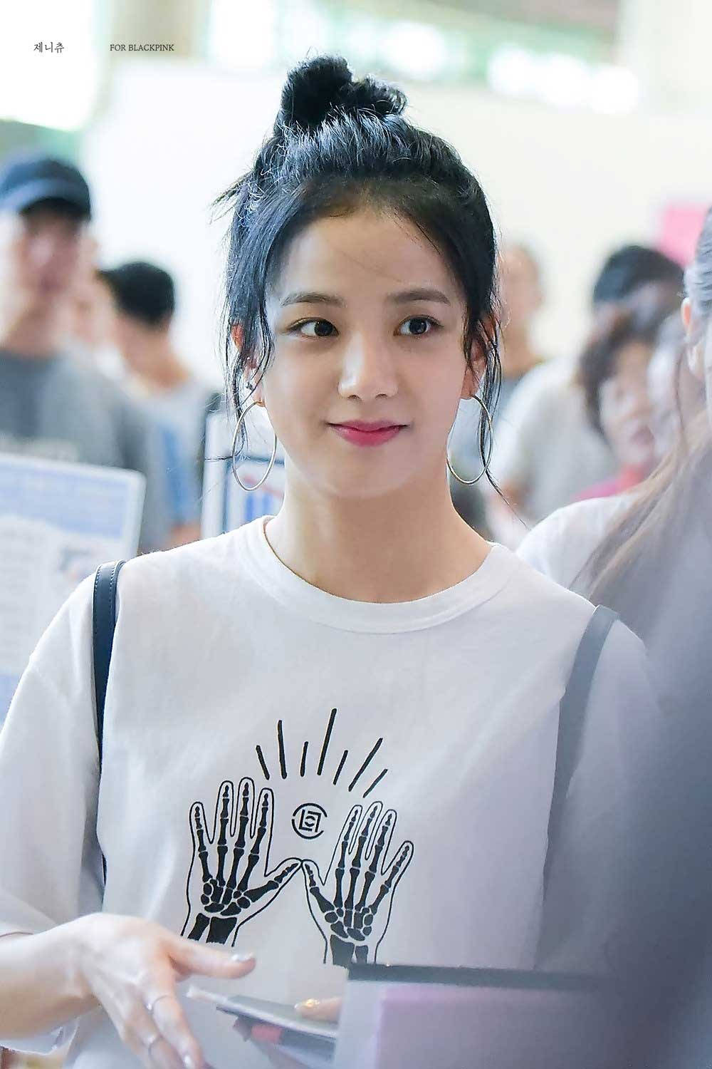 Jisoo Cute 桌布 壁紙 — 一位深色頭髮束成髮髻的年輕女性，穿著帶有黑色骷髏手圖案的白色T恤，溫柔地微笑。
