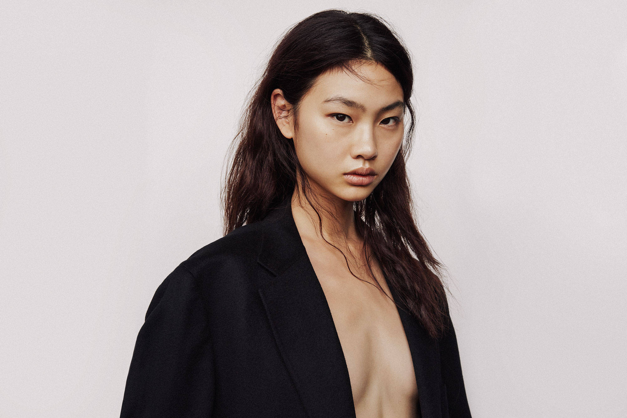 Hoyeon 桌布 壁紙 — 一位深色頭髮的優雅女士，在純白色背景前穿著一件敞開的黑色西裝外套。