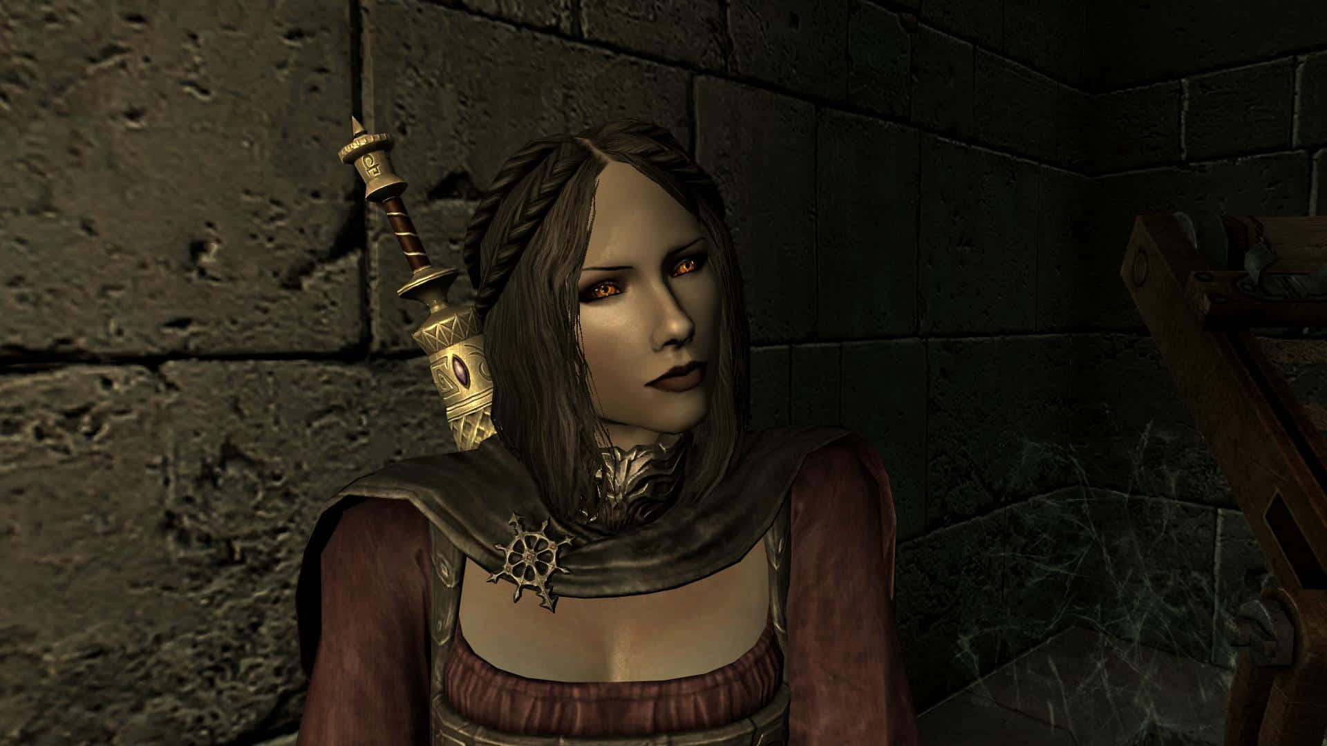 Skyrim Serana 桌布 壁紙 — 一位深色頭髮的奇幻戰士，擁有發光的紅色眼睛，站在石頭地牢中，背上背著一把劍。