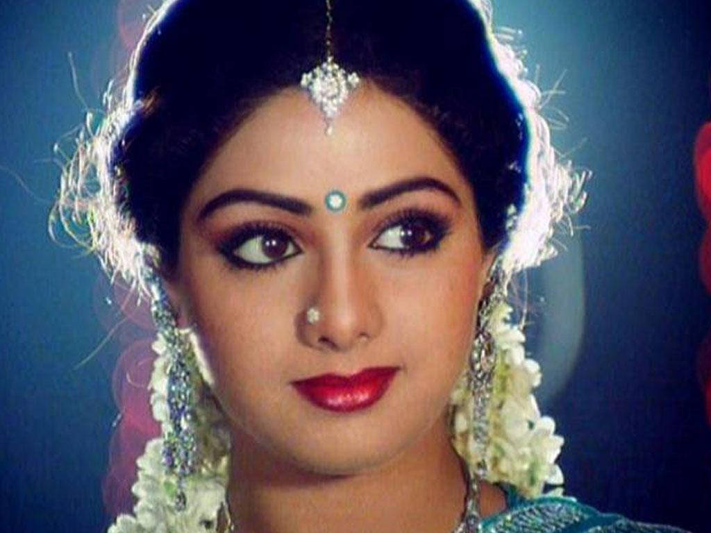 Sridevi 桌布 壁紙 — 一位深色頭髮的女性，佩戴珠寶和花朵，在深藍色背景下凝視著。