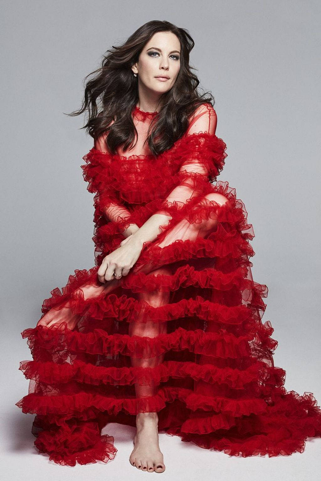 Fashion Model 桌布 壁紙 — 一位深色頭髮的女性，穿著寬大的紅色荷葉邊長袍，優雅地坐在中性灰色背景前。
