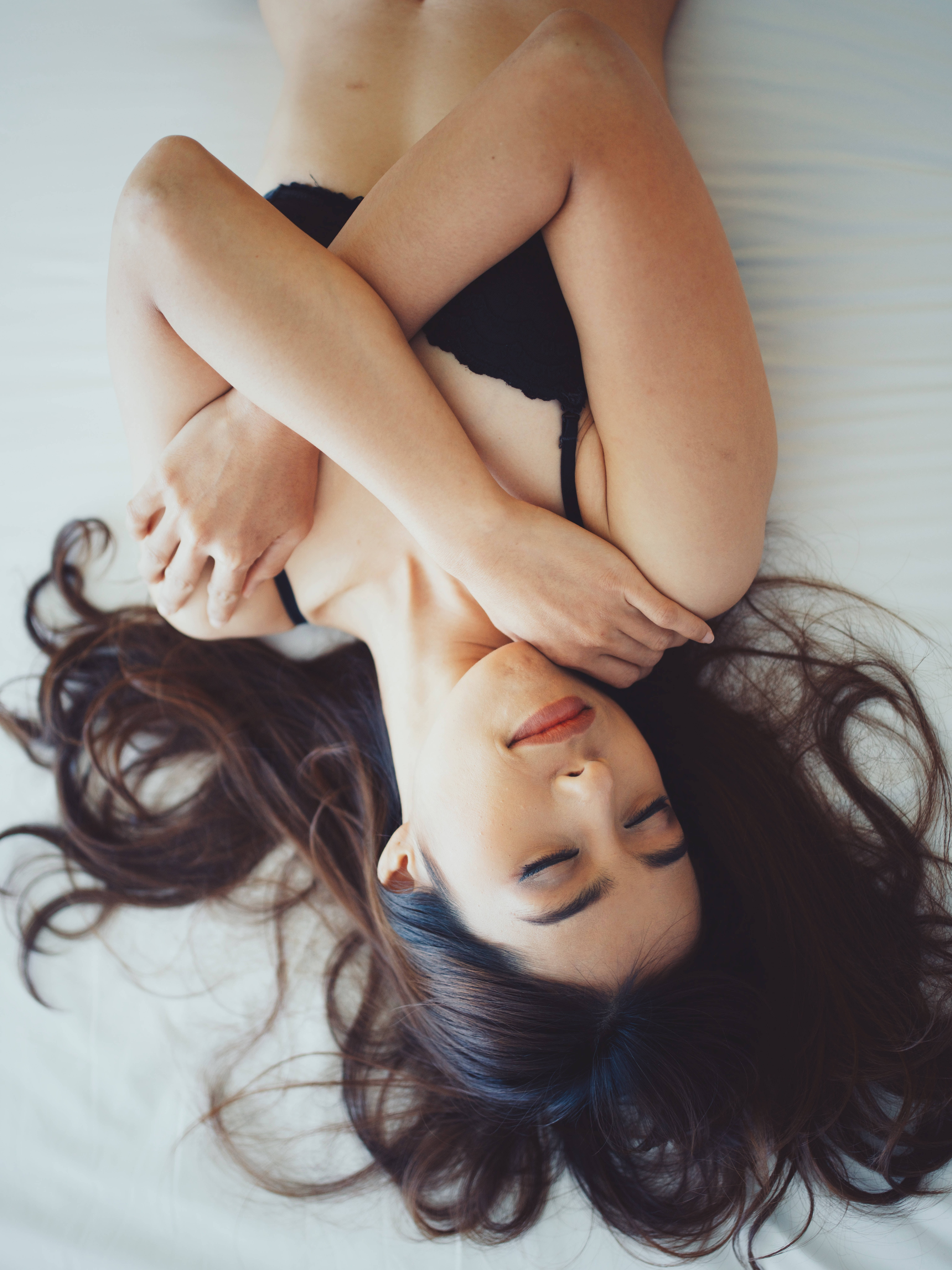 sexy lingerie 桌布 壁紙 — 一位深色頭髮的女性仰臥在白色床上，穿著黑色內衣，雙臂交叉在胸前，閉著眼睛安詳地休息。