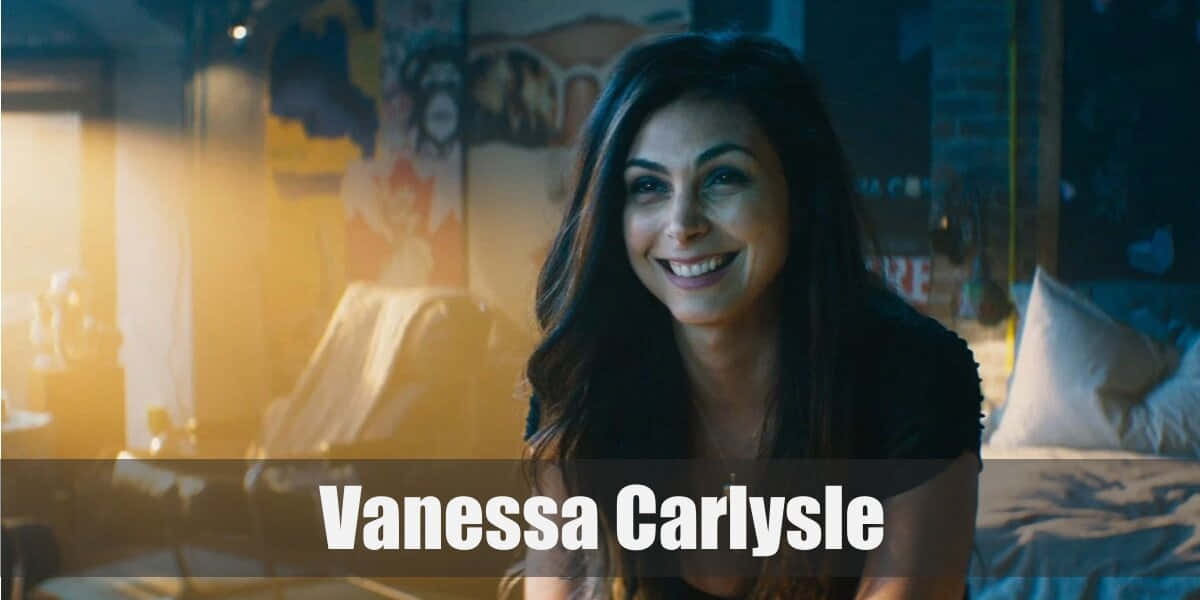 Vanessa Carlysle 桌布 壁紙 — 一位深色頭髮的女性在柔和光線的房間裡，溫暖的金色光芒和模糊的背景裝飾中，露出溫暖的笑容。