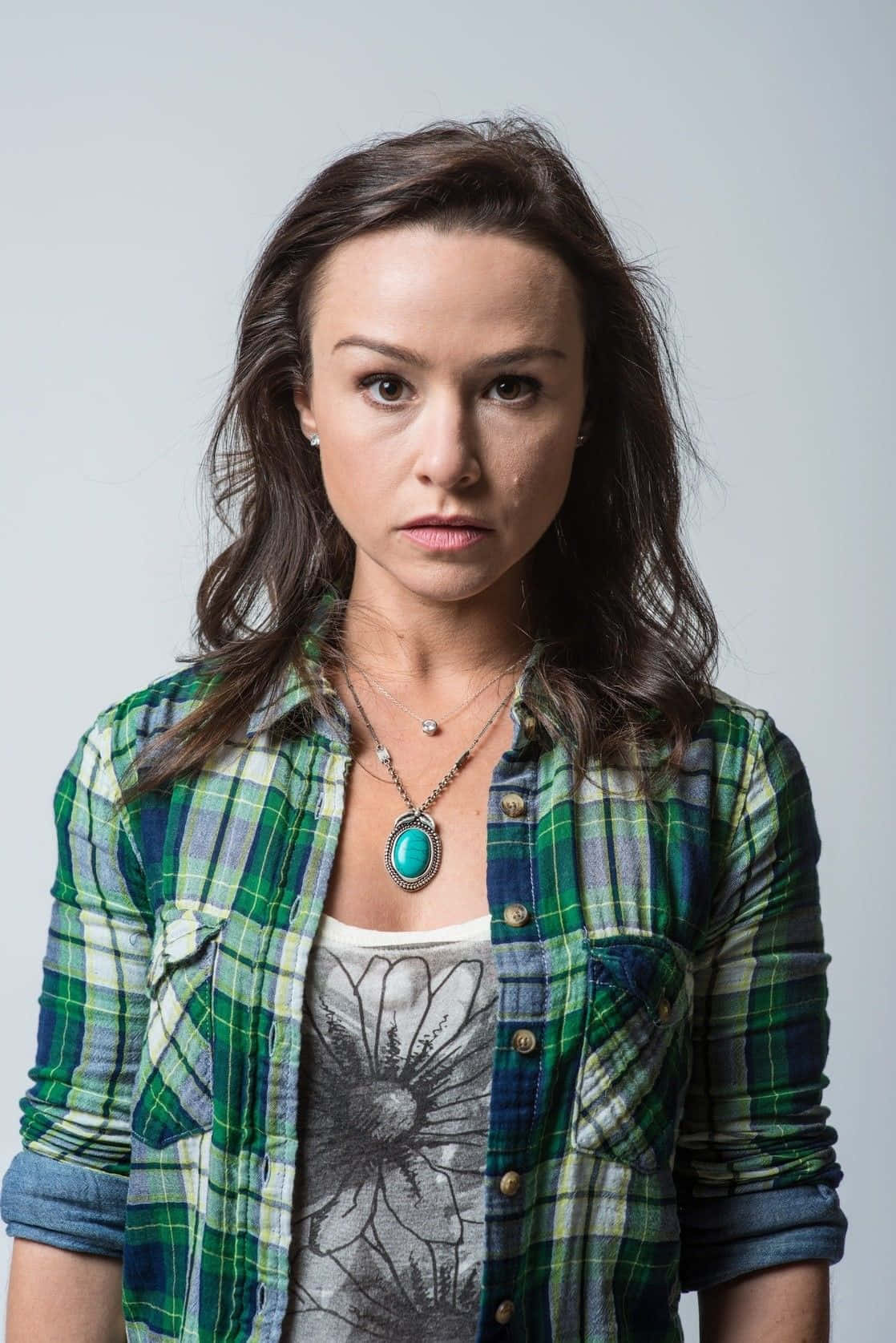 Danielle Harris 桌布 壁紙 — 一位深色頭髮的女性在純灰色背景前，穿著一件綠色格子襯衫，內搭花卉圖案T恤。
