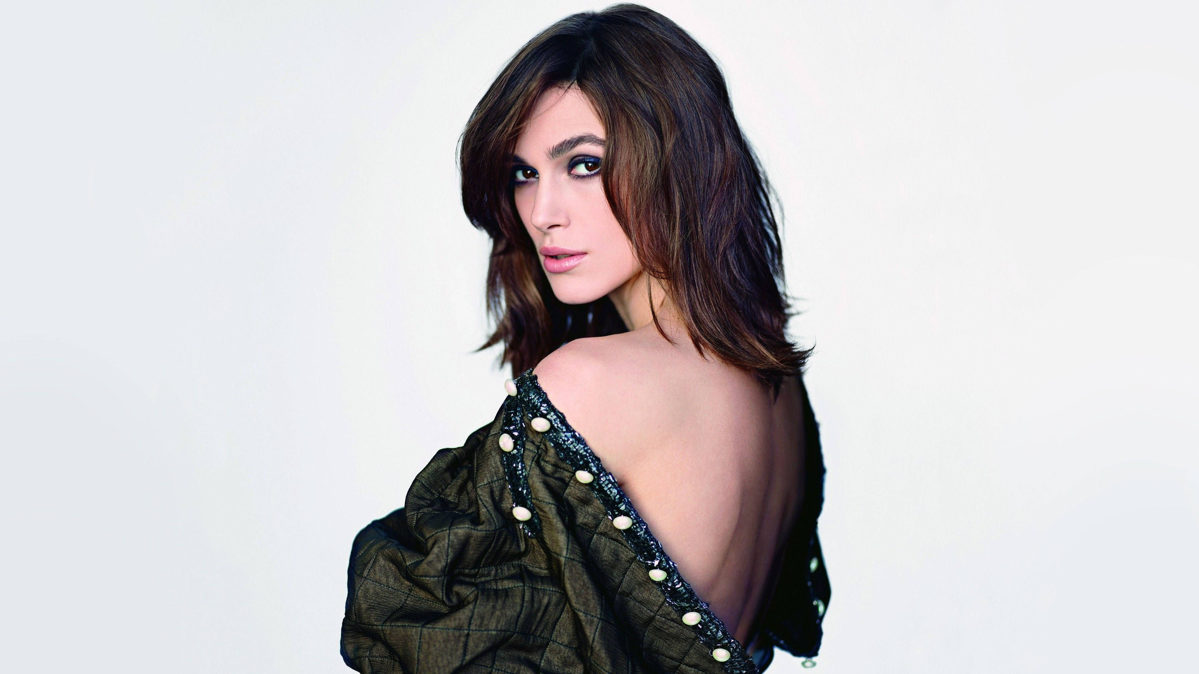 Keira Knightley 桌布 壁紙 — 一位深色頭髮的女性在純白色背景前，穿著深綠色珠飾露肩上衣，轉頭越過肩膀。