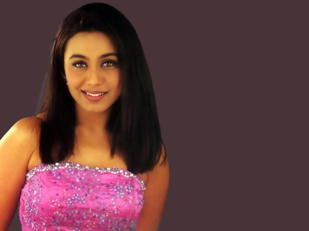 Rani Mukerji 桌布 壁紙 — 一位深色頭髮的女性在純紫色背景前，穿著閃亮的粉紅色無肩帶連衣裙，溫暖地微笑。