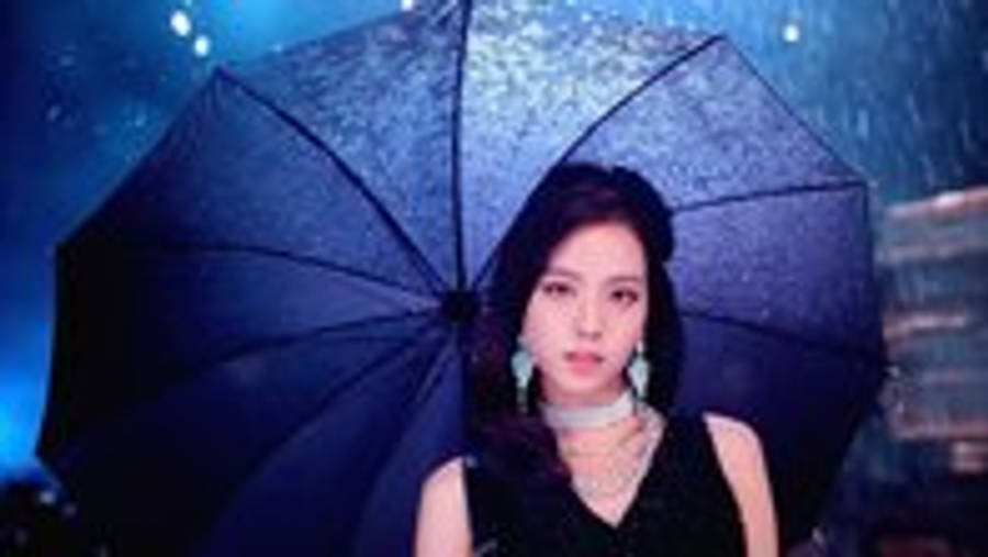 BLACKPINK 桌布 壁紙 — 一位深色頭髮的女性在雨中，在藍色調的城市燈光下撐著一把黑色雨傘。