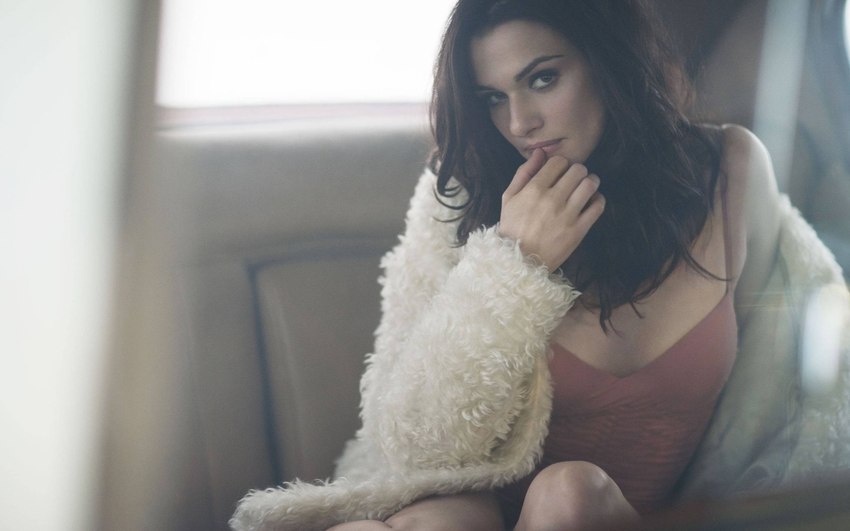 Rachel Weisz 桌布 壁紙 — 一位深色頭髮的女性坐在車裡，穿著蓬鬆的白色外套和粉紅色上衣，若有所思地看著相機。