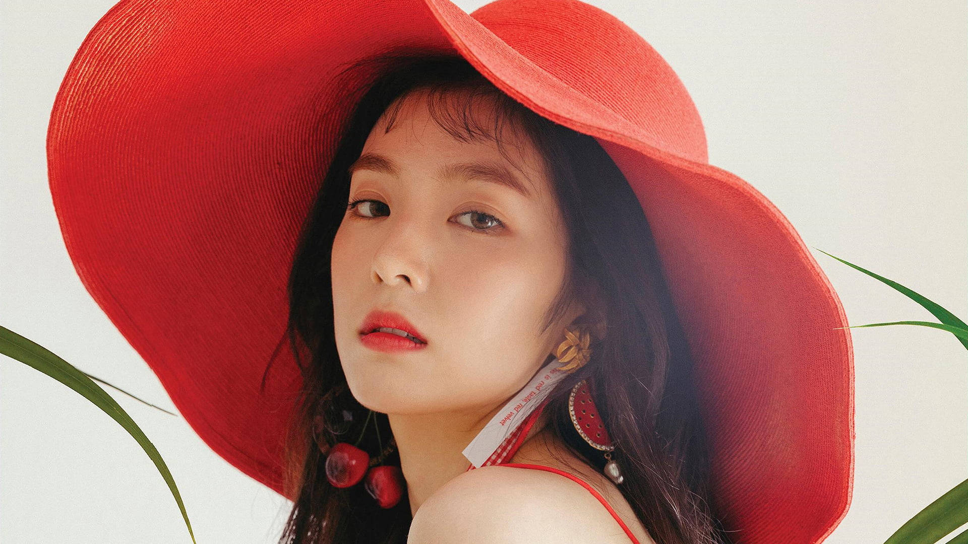 irene 桌布 壁紙 — 一位深色頭髮的女性戴著一頂大膽的紅色寬邊帽，搭配紅色唇膏，背景是柔和的白色和綠色葉子。