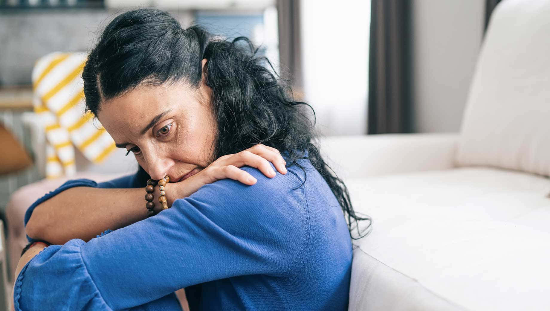 Depressed 桌布 壁紙 — 一位深色頭髮的女性穿著藍色襯衫蜷縮在沙發上，臉埋在手臂中，顯示出痛苦。