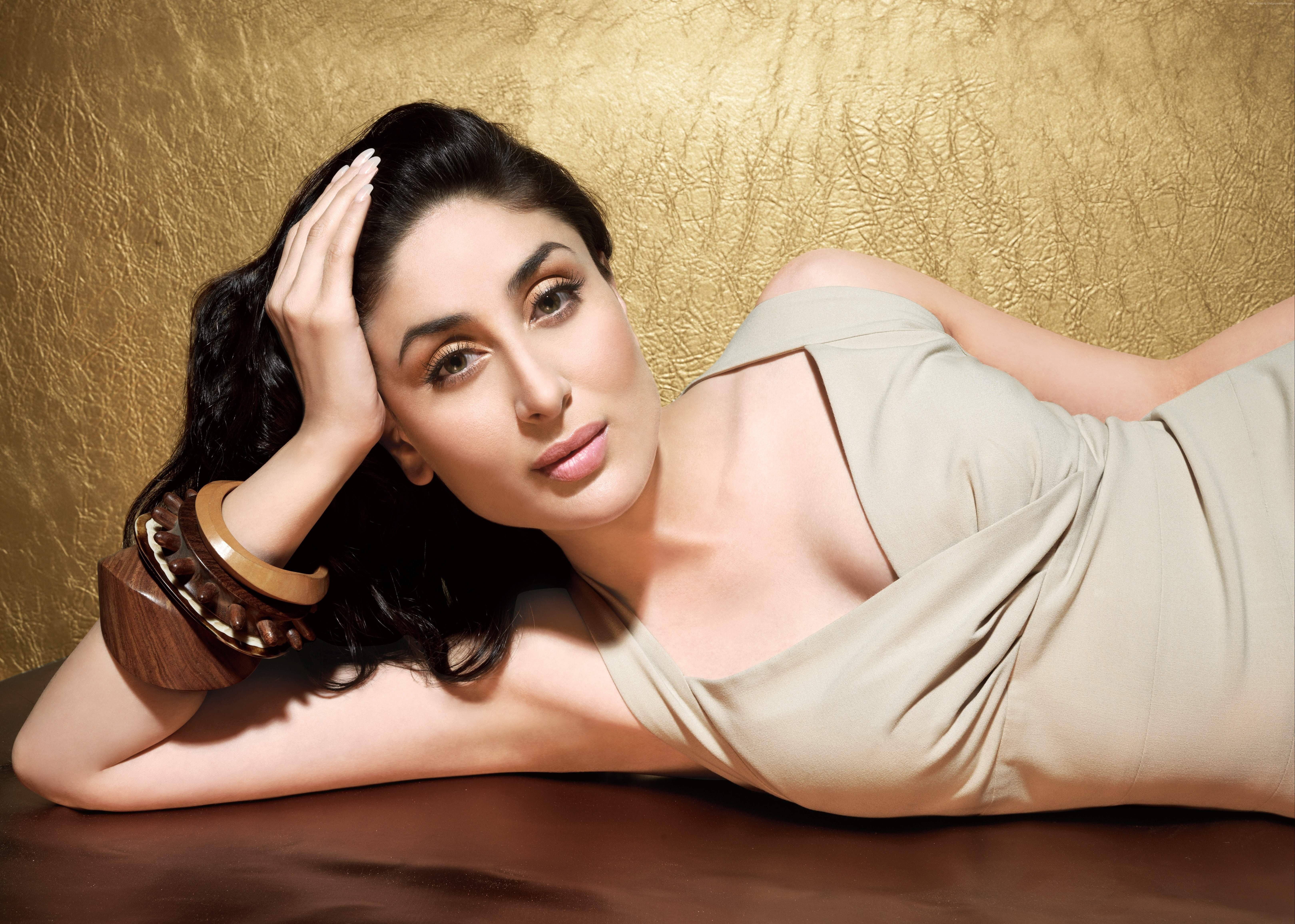 Kareena 桌布 壁紙 — 一位深色頭髮的女性躺在木質表面上，背景是帶有紋理的金色背景，身穿米色連衣裙和木質手鐲，直視鏡頭。