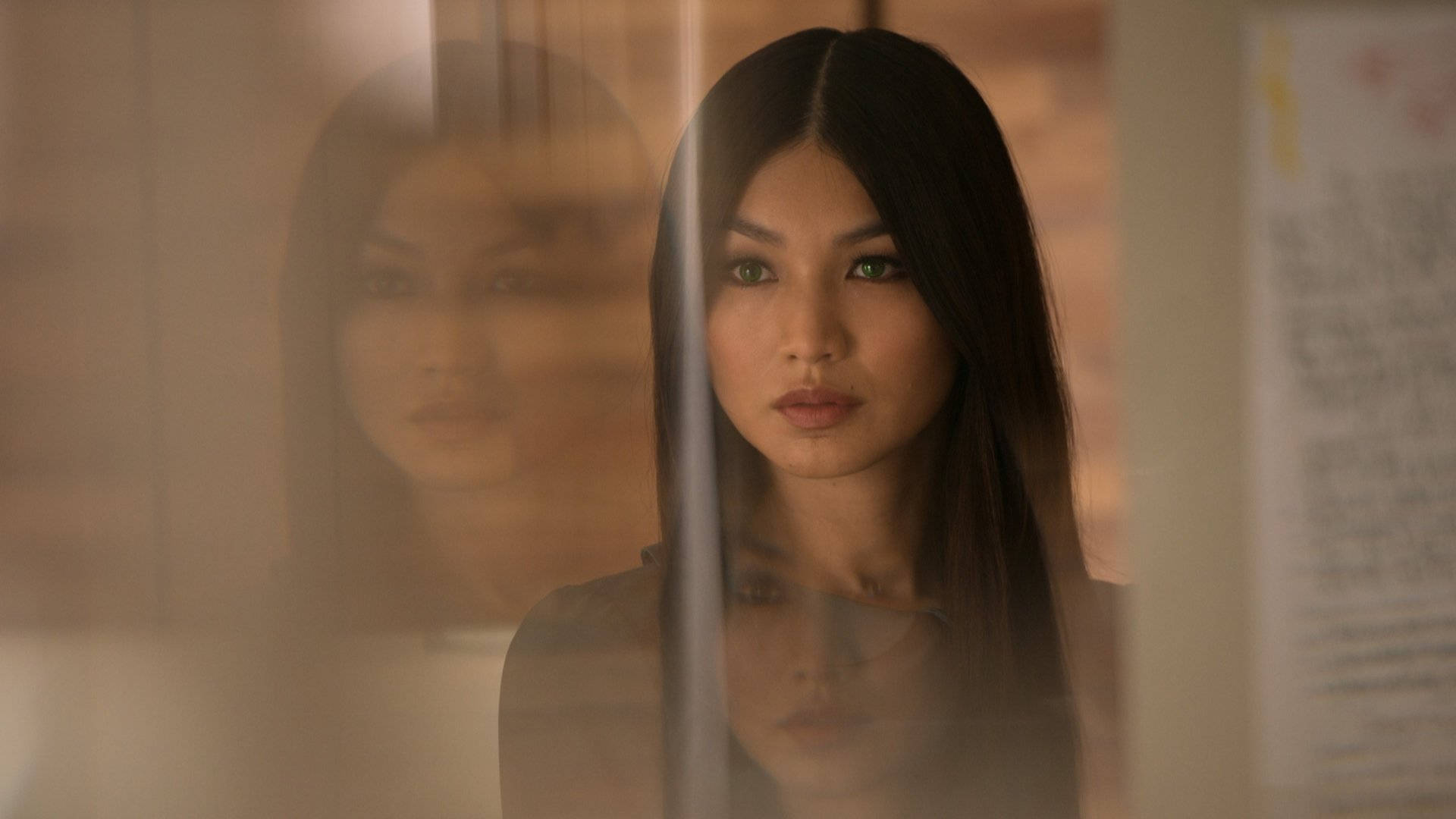 Gemma Chan 桌布 壁紙 — 一位深色頭髮的女性透過煙霧玻璃專注地凝視，身後層疊著模糊的倒影。