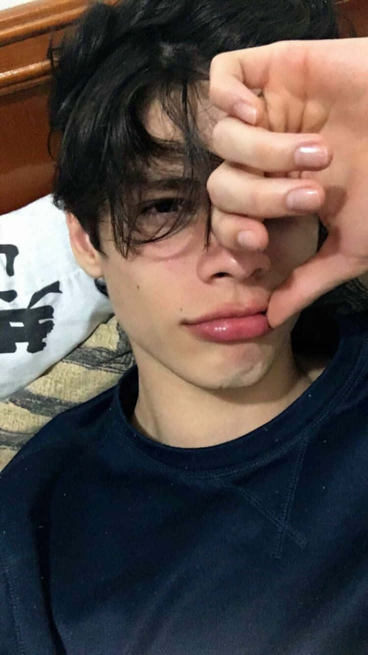 美少年動態圖 桌布 壁紙 — 一位深色頭髮的年輕人躺在圖案沙發上，將手放在一隻眼睛上，穿著深藍色襯衫。