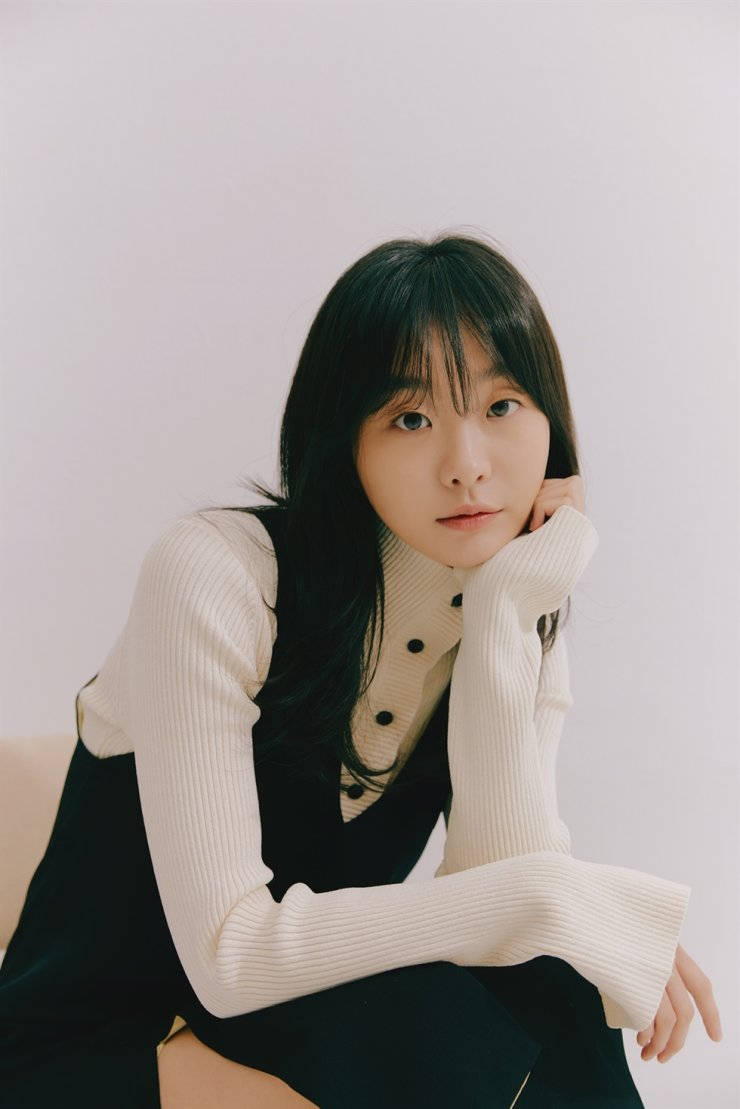 Beloved 桌布 壁紙 — 一位深色頭髮的年輕女子，身穿米色羅紋毛衣和黑色背心，在純白背景上將下巴擱在手上。