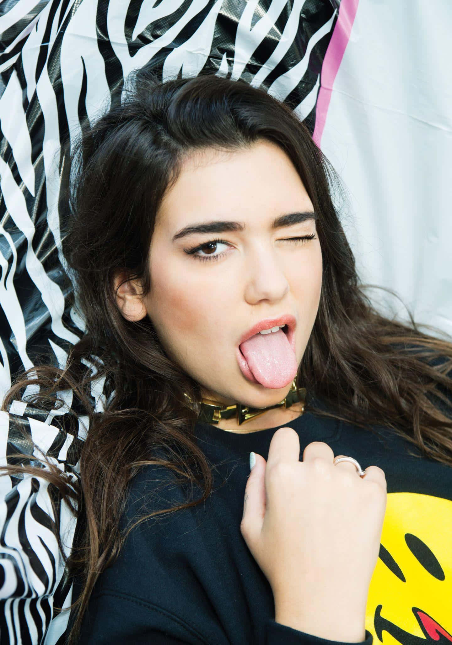 Dua Lipa 桌布 壁紙 — 一位深色頭髮的年輕女子在搶眼的斑馬紋背景前頑皮地伸出舌頭。