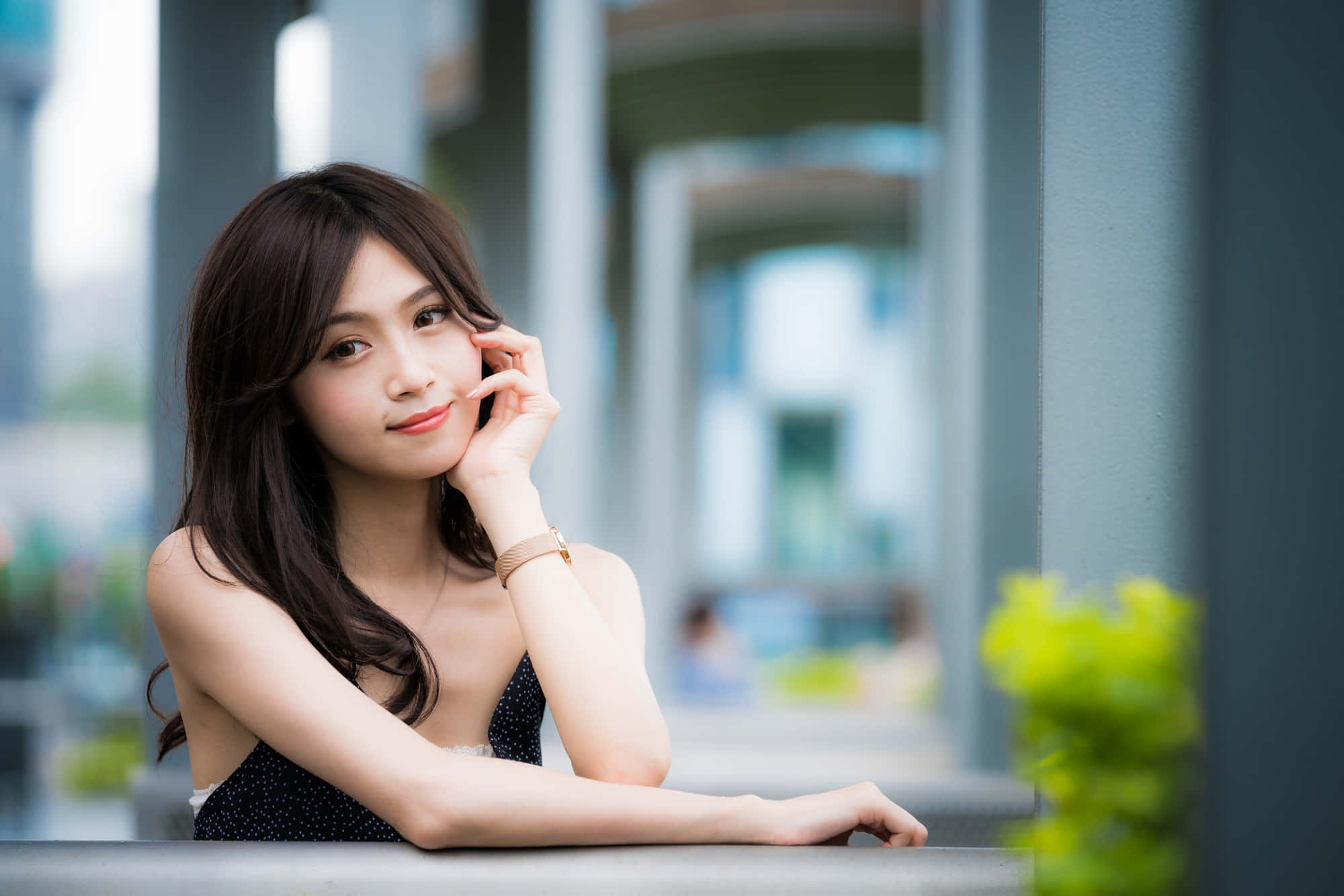 美女 桌布 壁紙 — 一位深色頭髮的年輕女子在現代都市環境中，將下巴擱在手上，靠在欄杆上。