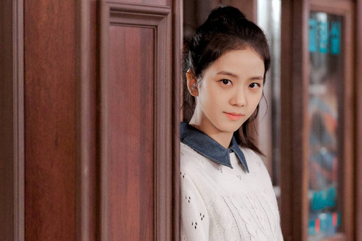 drama 桌布 壁紙 — 一位深色頭髮的年輕女子從木門後探頭，身穿白色針織毛衣配牛仔布領。