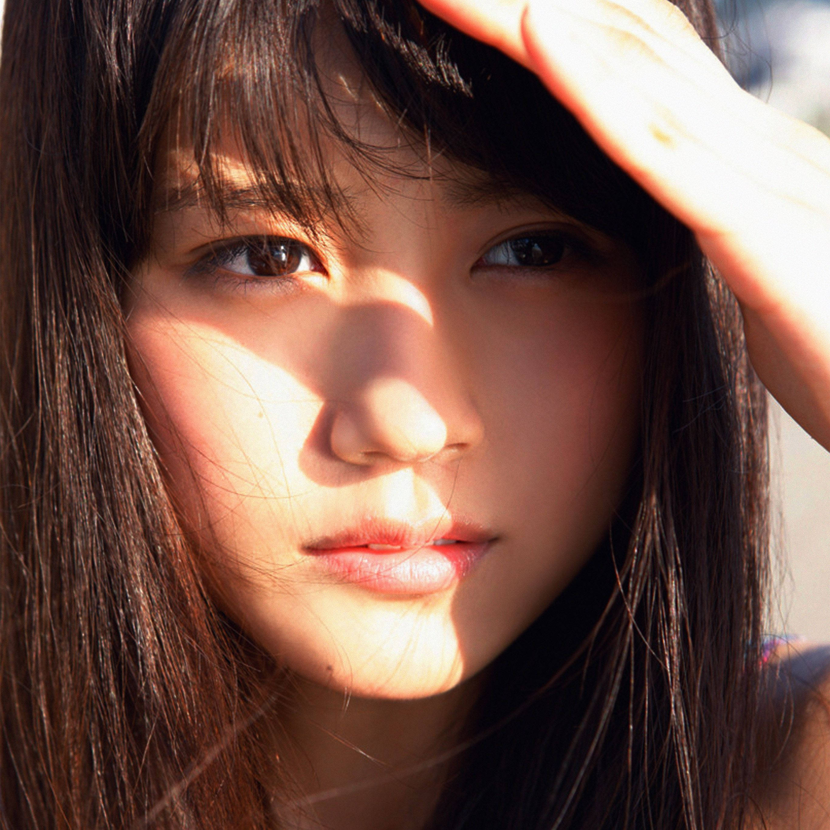 Face 桌布 壁紙 — 一位深色頭髮的年輕女子用手遮擋刺眼的陽光，陽光在她臉上投下柔和的陰影。