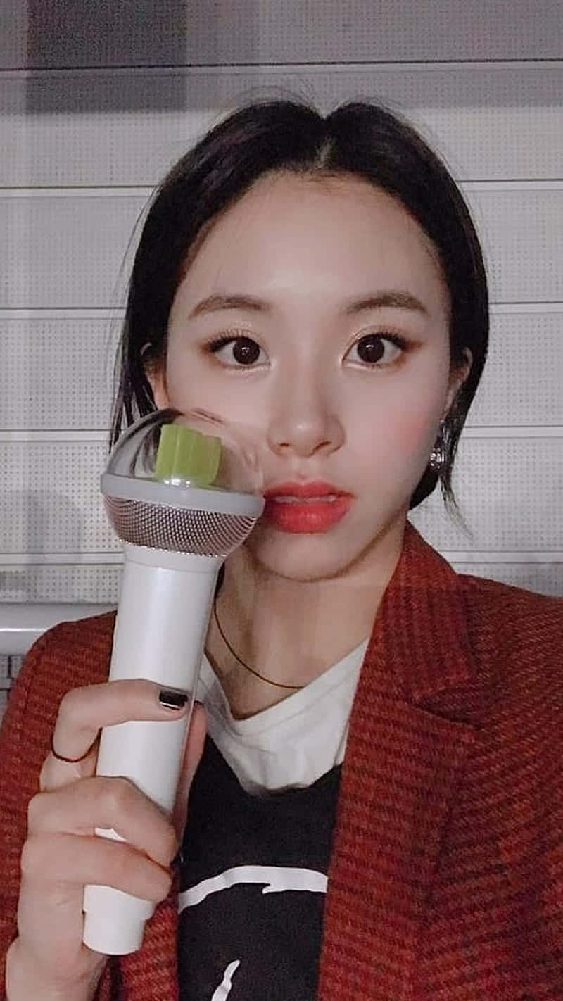 chaeyoung 桌布 壁紙 — 一位深色頭髮的年輕女性，在灰色瓷磚牆前將白色麥克風靠近臉部。