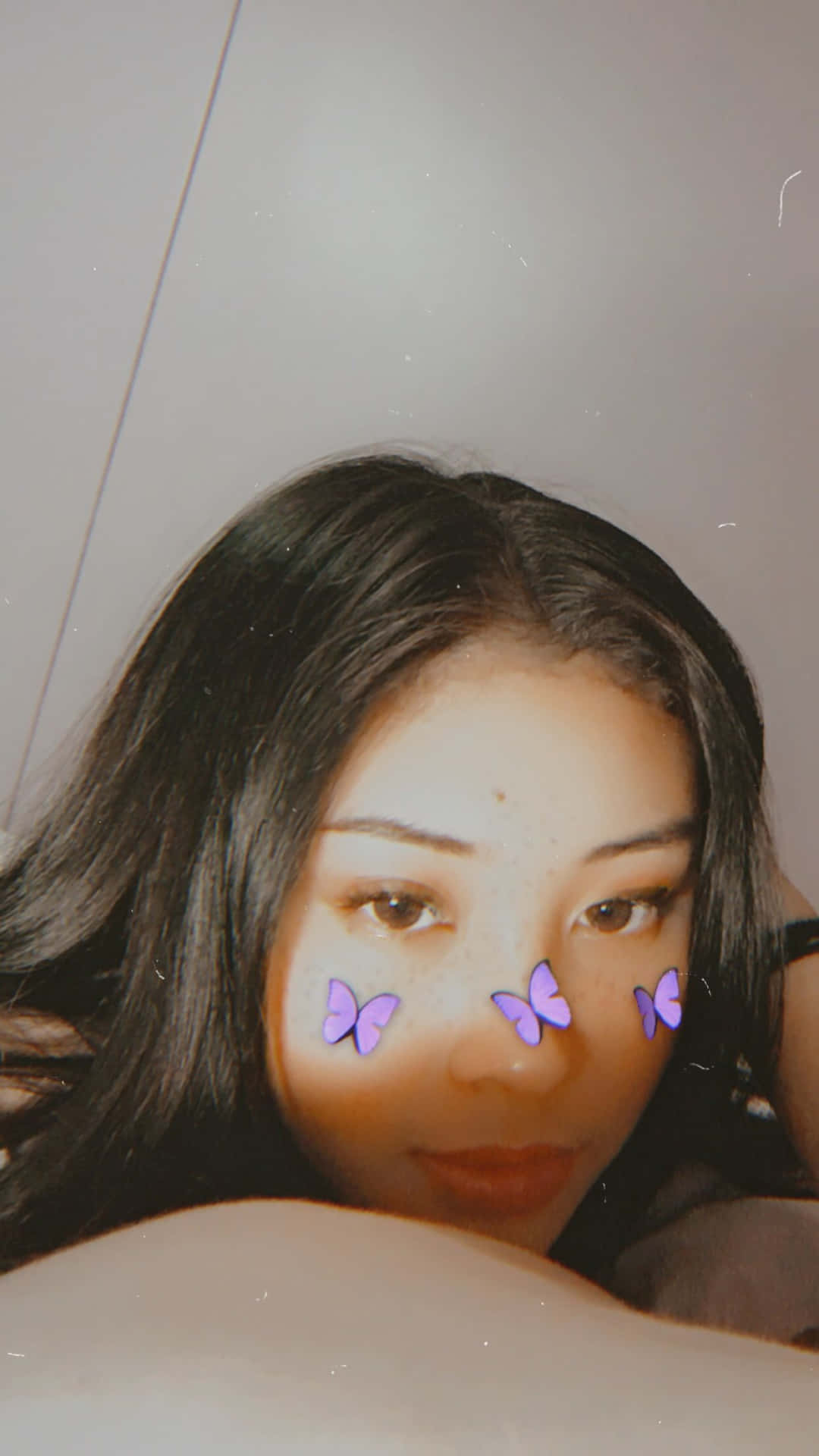 Snapchat 桌布 壁紙 — 一位深色頭髮的年輕女性，在素色牆壁背景下，臉頰上數位放置了三隻紫色蝴蝶。