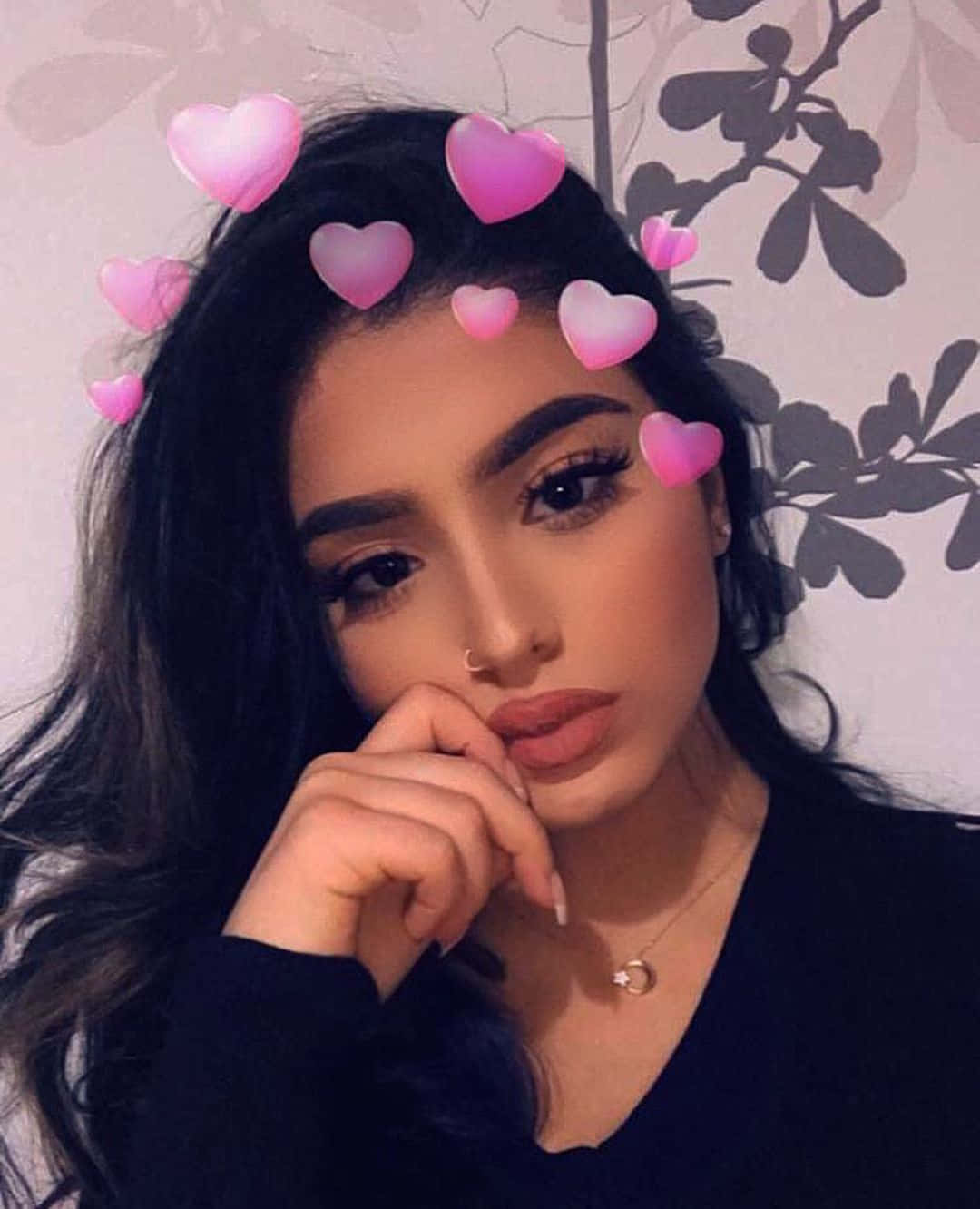 Snapchat 桌布 壁紙 — 一位深色頭髮的年輕女性，帶著粉紅色心形濾鏡，在花卉壁紙背景前若有所思地擺姿勢。