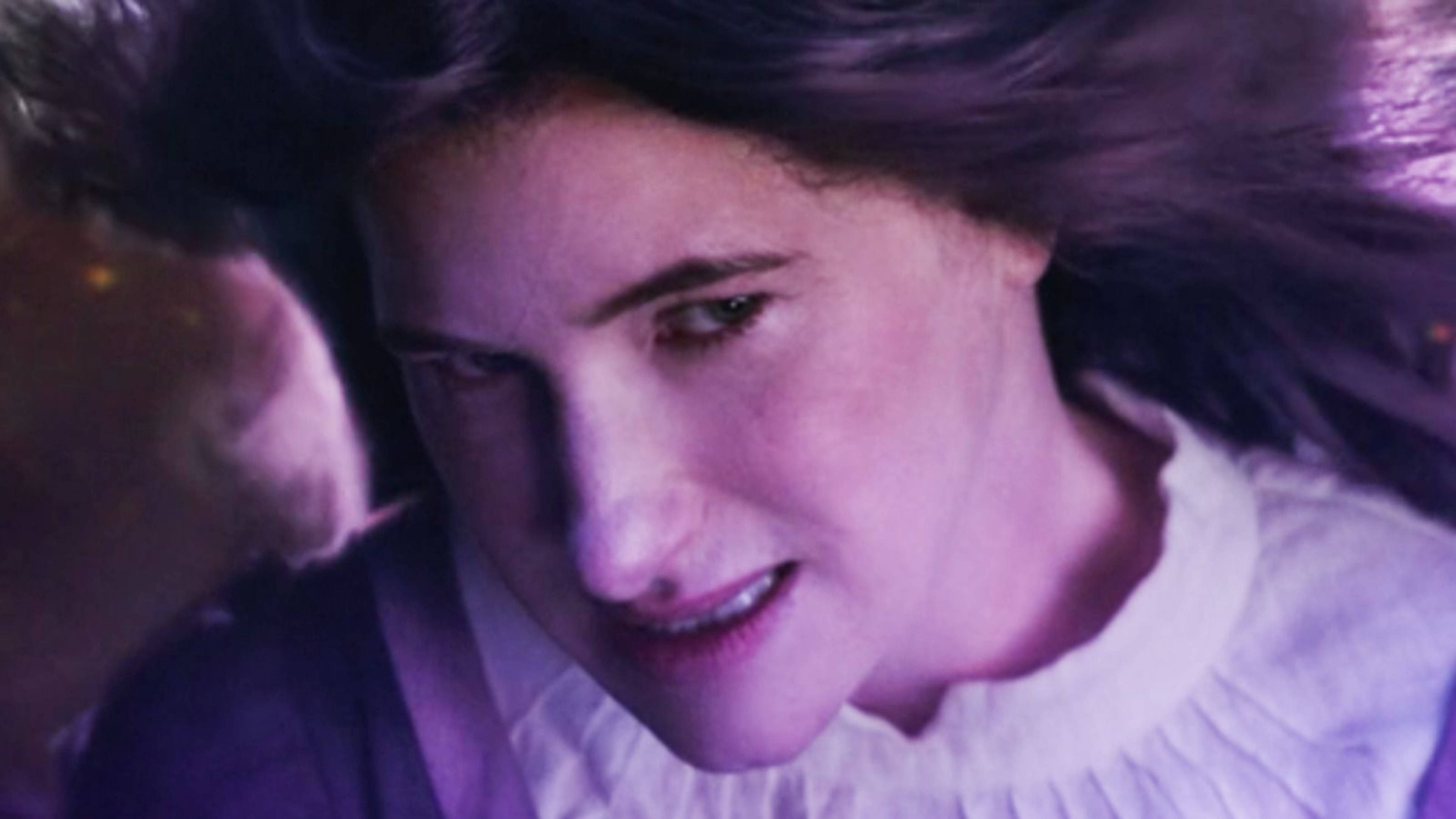 Agatha Harkness 桌布 壁紙 — 一位深色頭髮的年輕女性在紫色燈光下溫柔微笑，頭髮周圍有動態模糊效果。
