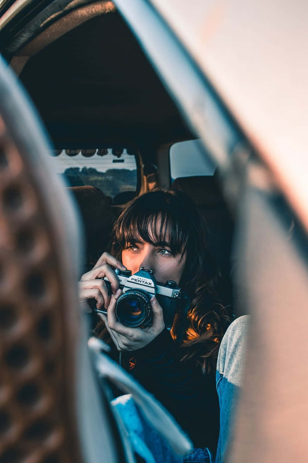 Holding Camera 桌布 壁紙 — 一位深色頭髮的年輕女性在黃金時刻坐在車內，將銀色Pentax底片相機舉到眼前。