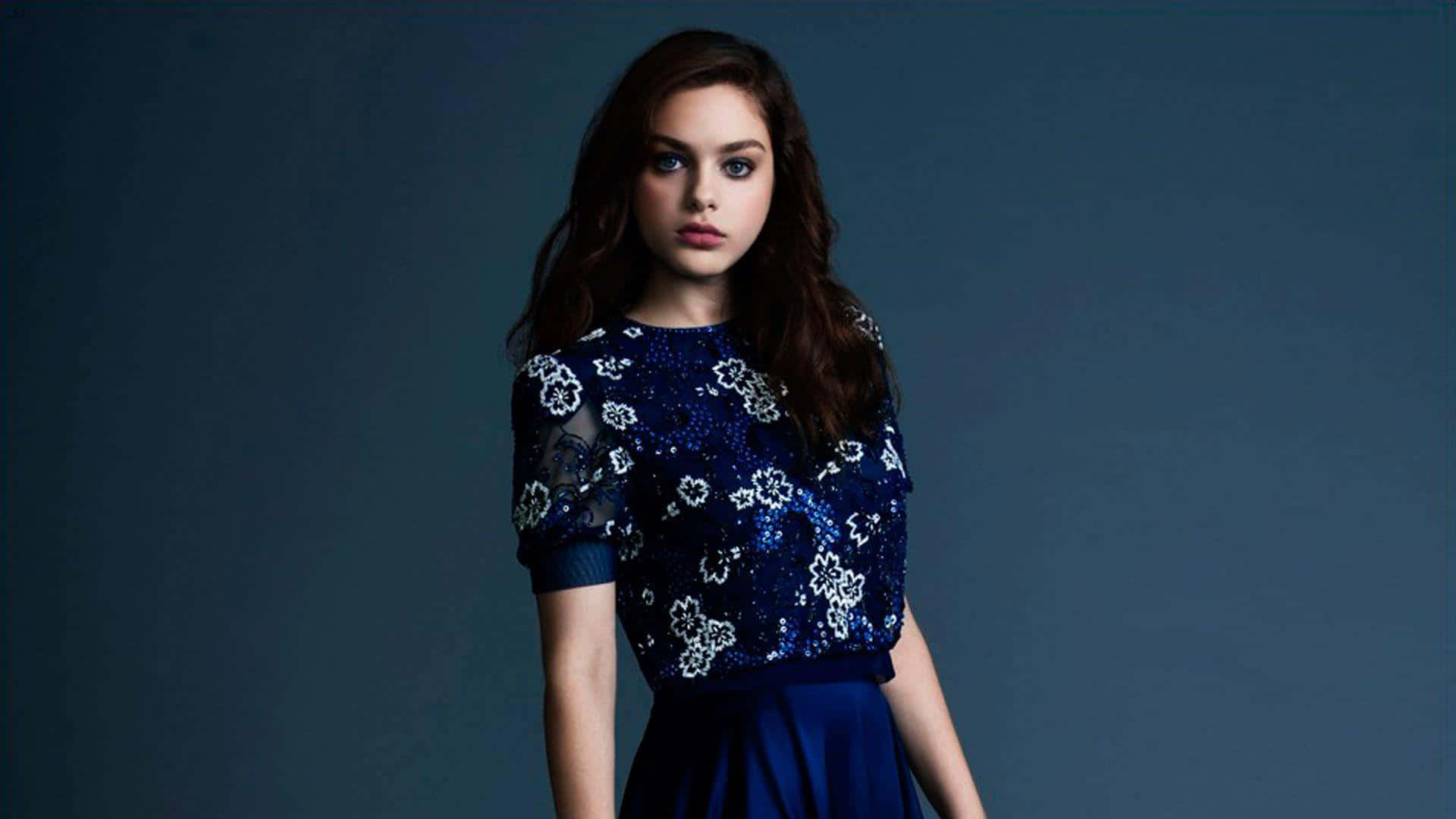 Odeya Rush 桌布 壁紙 — 一位深色頭髮的年輕女性穿著藍色亮片上衣，帶有白色花卉圖案，背景為純深藍色。