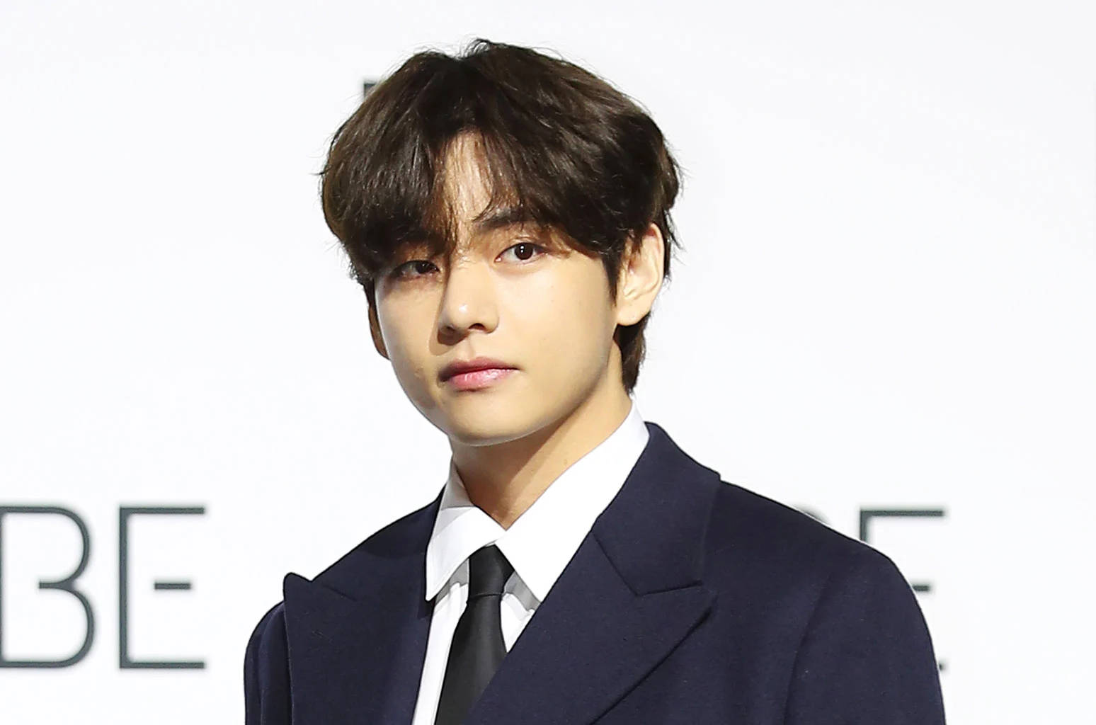 BTS 桌布 壁紙 — 一位深色頭髮的年輕男士穿著俐落的海軍藍西裝和黑色領帶，背景是純白色。