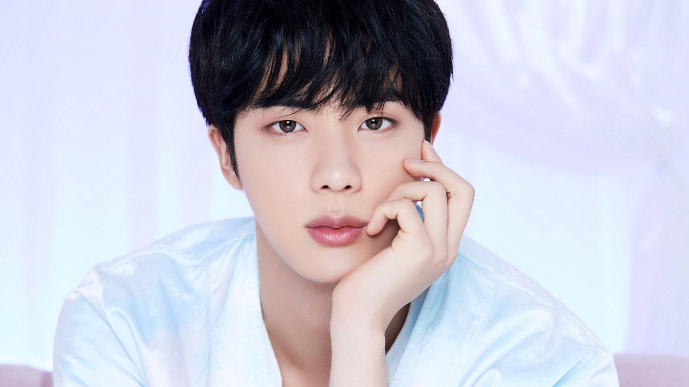 kim seok jin 桌布 壁紙 — 一位深色頭髮的年輕男子，在柔和的淺藍色背景上，將下巴擱在手上。