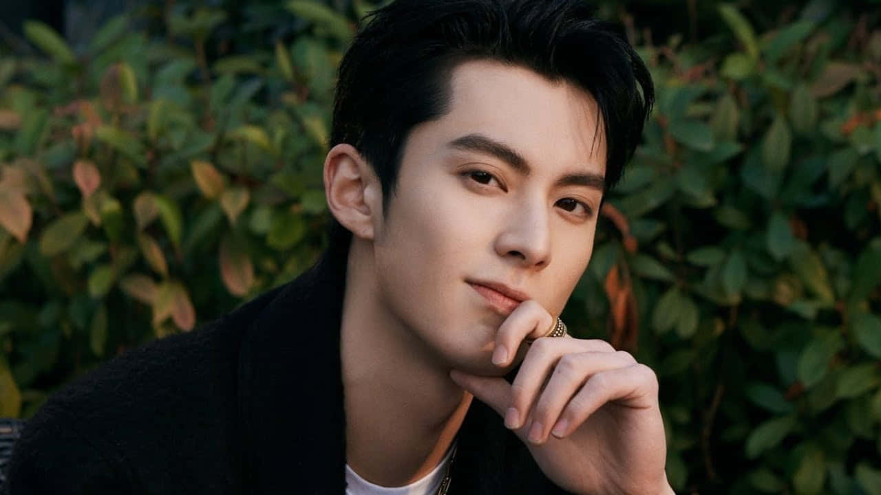 Dylan Wang 桌布 壁紙 — 一位深色頭髮的年輕男子，表情若有所思，手托下巴，背景是茂密的綠色樹葉。