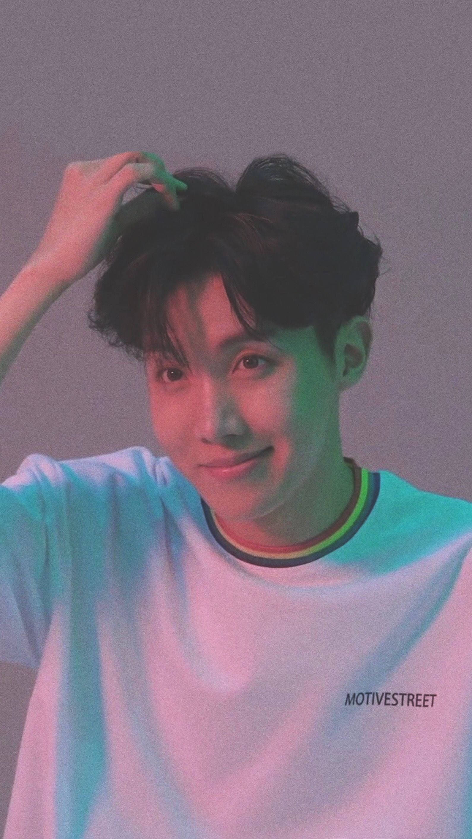 jhope 桌布 壁紙 — 一位深色頭髮的年輕男子在充滿活力的粉紅色和綠色攝影棚燈光下輕觸頭部，溫柔微笑。