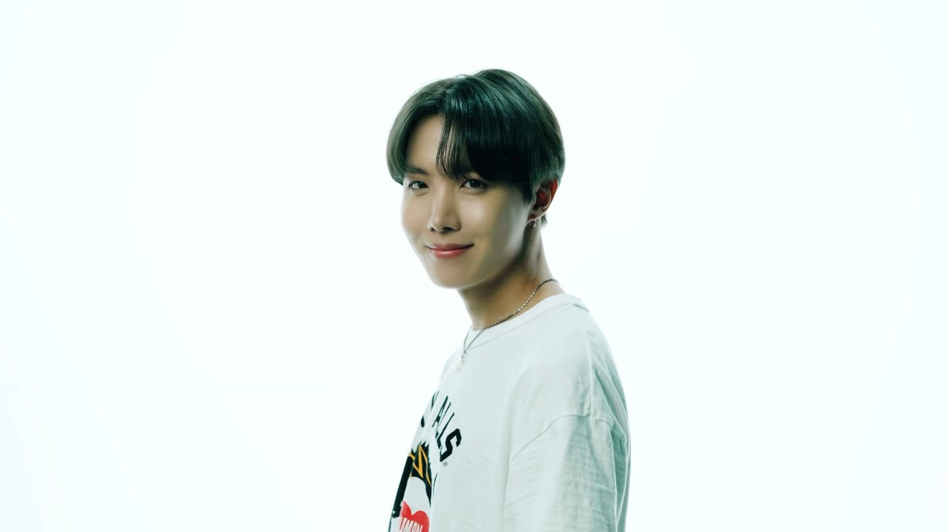j-hope 桌布 壁紙 — 一位深色頭髮的年輕男子在明亮的白色背景前穿著白色圖案T恤，溫柔地微笑。