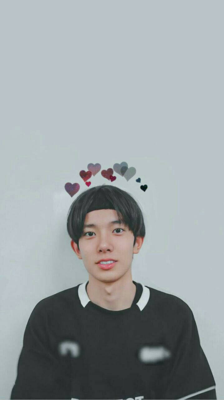 Kpop Aesthetic 桌布 壁紙 — 一位深色頭髮的年輕男子在純灰色背景前溫柔微笑，頭頂上漂浮著一個由彩色心形組成的皇冠。