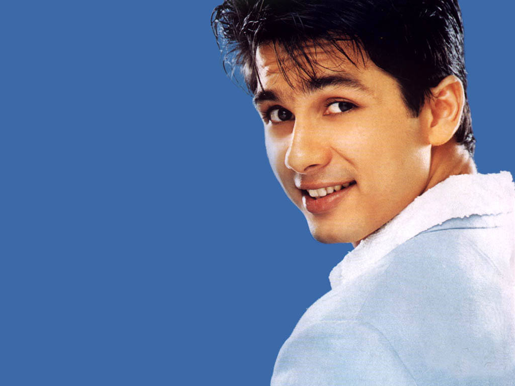 Shahid Kapoor 桌布 壁紙 — 一位深色頭髮的年輕男子在純藍色背景上越過肩膀溫暖地微笑。