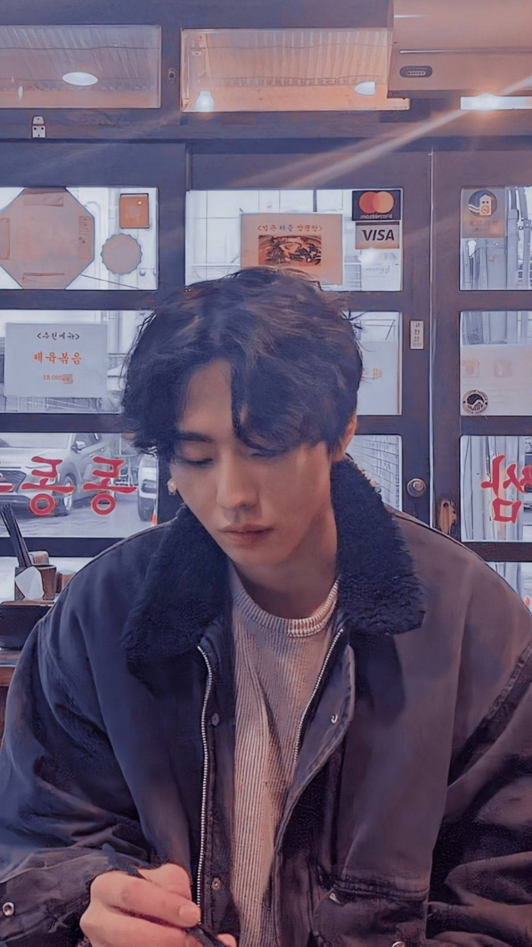 Ahn Hyo Seop 桌布 壁紙 — 一位深色頭髮的年輕男子坐在燈光溫暖的咖啡館裡，穿著一件有毛絨領的深色外套，若有所思地低頭看著。