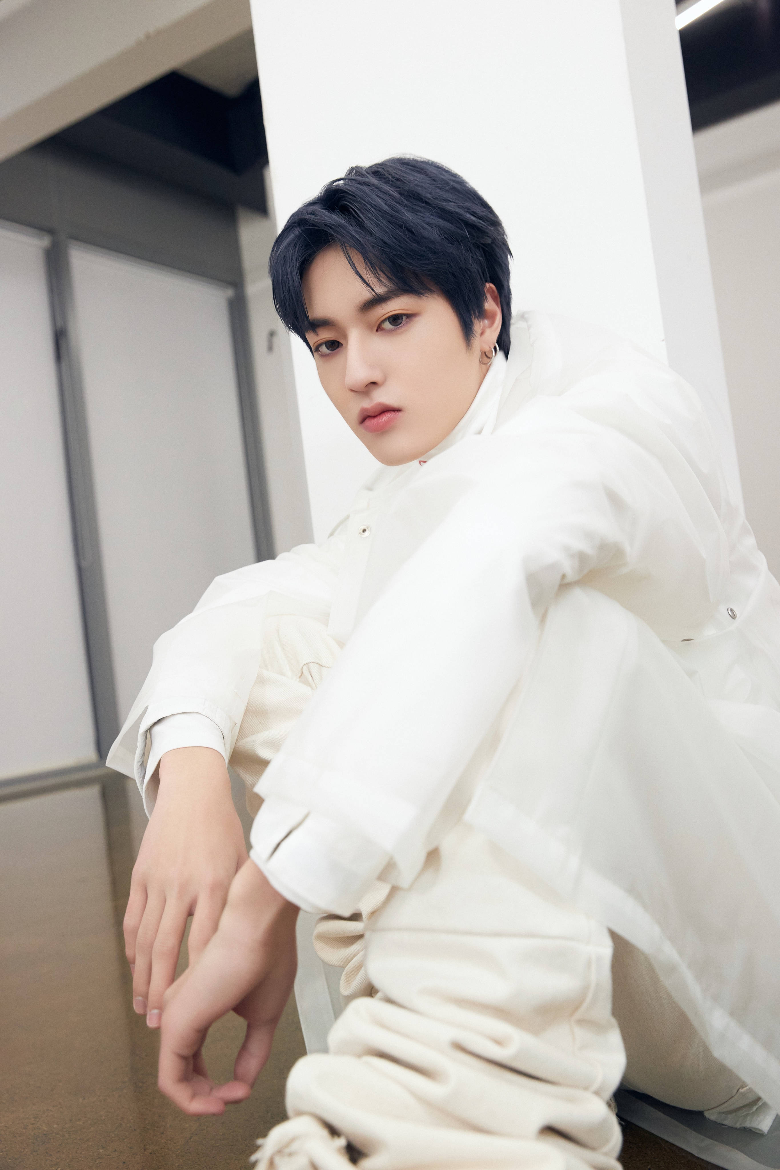 Haruto 桌布 壁紙 — 一位深色頭髮的年輕男子坐在現代室內空間，靠著白色柱子，身穿寬鬆白色服裝。
