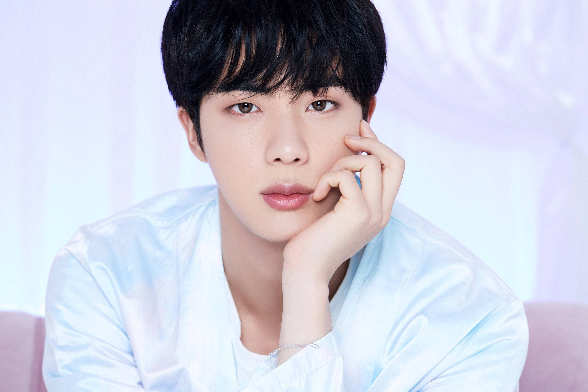 kim seok jin 桌布 壁紙 — 一位深色頭髮的年輕男子將下巴擱在手上，背景是柔和的粉彩色。