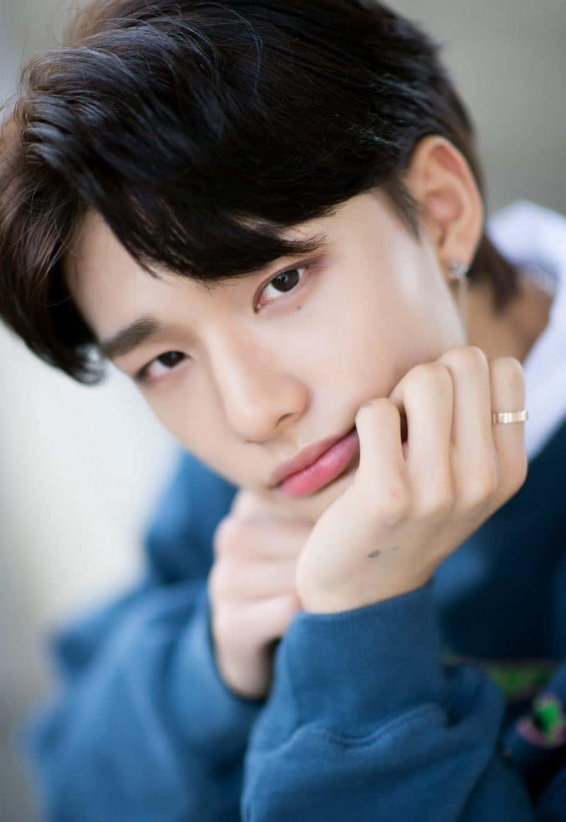 hyunjin 桌布 壁紙 — 一位深色頭髮的年輕男子將下巴擱在手上，溫柔地凝視鏡頭，身穿藍色連帽衫並戴著金戒指。