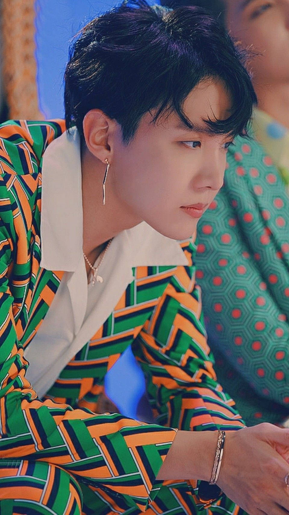 j-hope 桌布 壁紙 — 一位深色頭髮的年輕男子穿著大膽的綠橙條紋襯衫和銀飾，若有所思地看向一旁。