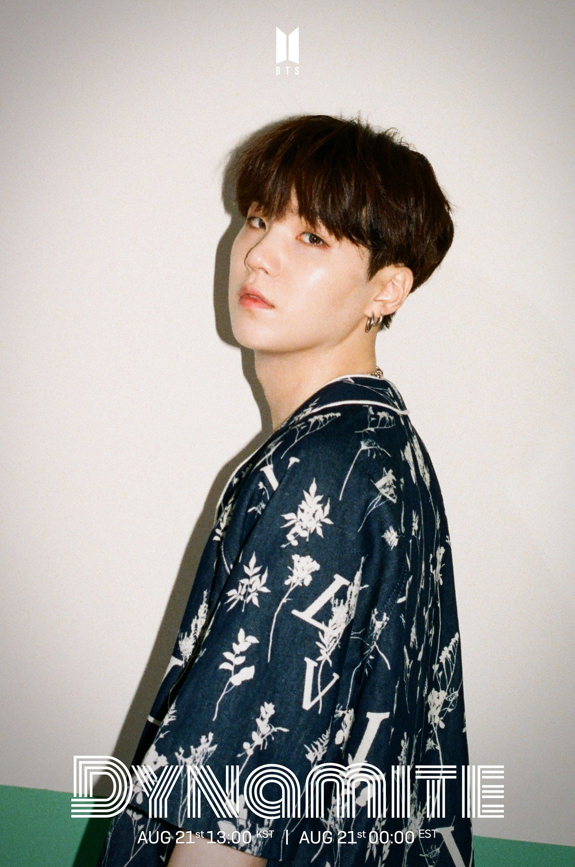 Suga Bts 桌布 壁紙 — 一位深色頭髮的年輕男子穿著花卉圖案襯衫，在柔和燈光和文字疊加的素色牆壁前擺姿勢。