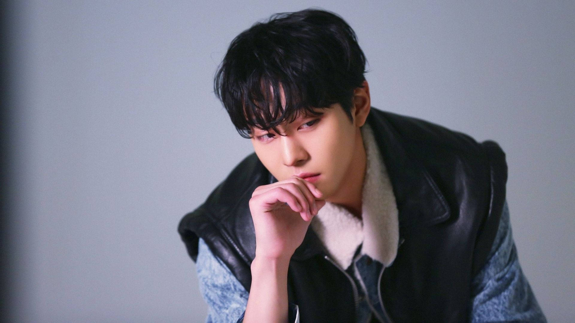 Ahn Hyo Seop 桌布 壁紙 — 一位深色頭髮的年輕男子穿著黑色皮背心，內搭牛仔襯衫，將下巴擱在手上，背景為純灰色。