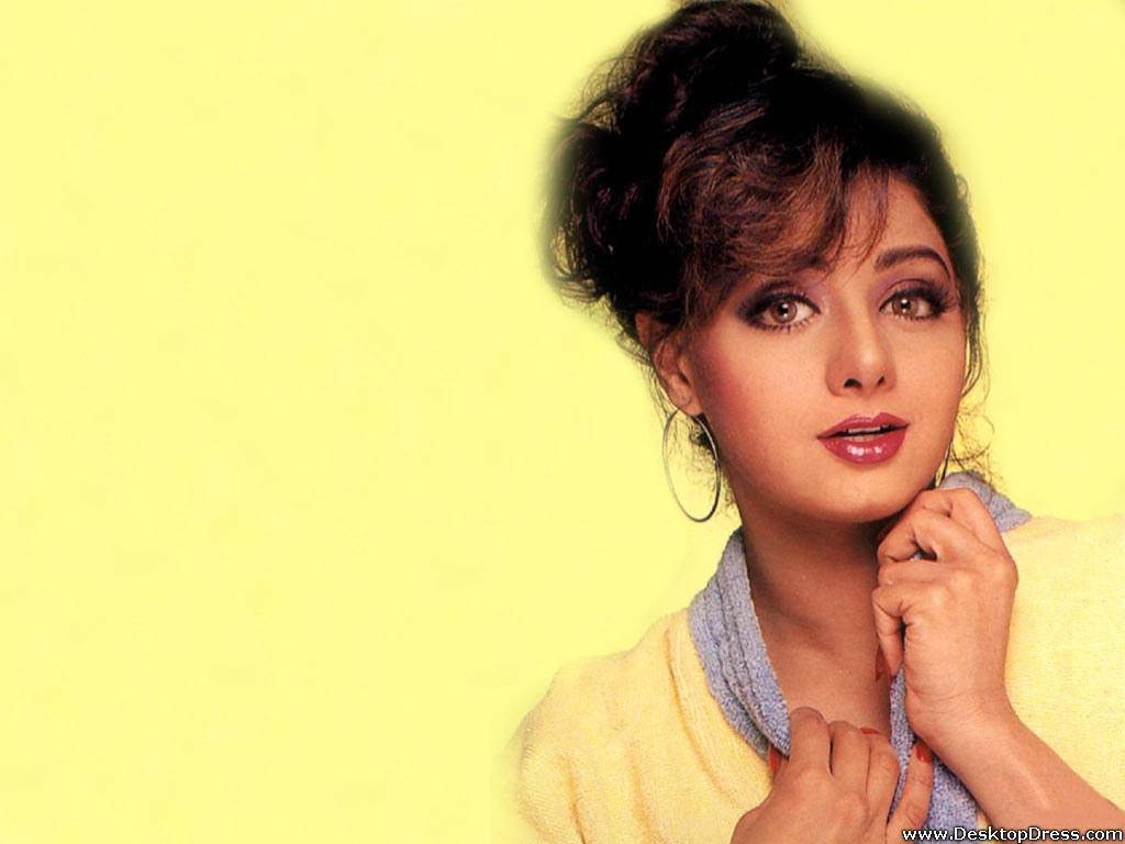 Sridevi 桌布 壁紙 — 一位深色頭髮盤成髮髻、戴著圓環耳環的女性，在純黃色背景前溫柔地凝視。