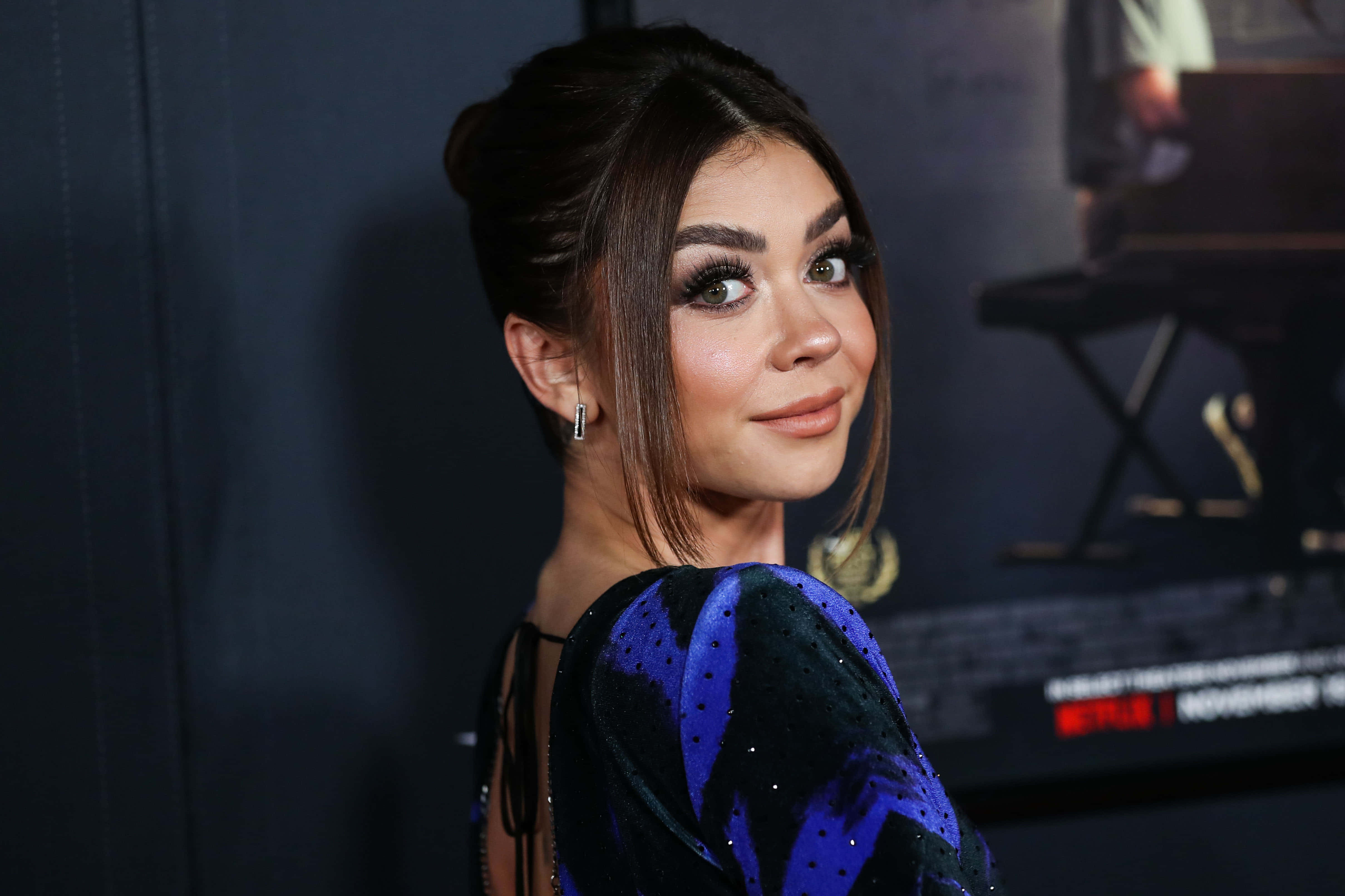 Sarah Hyland 桌布 壁紙 — 一位深色頭髮盤起、身穿藍色亮片連衣裙的女性轉頭越過肩膀看向相機。