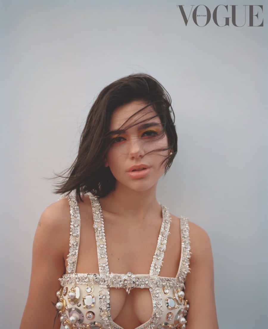 Dua Lipa 桌布 壁紙 — 一位深色頭髮被風吹拂的女性，在純灰色背景前穿著閃閃發光的珠寶上衣。