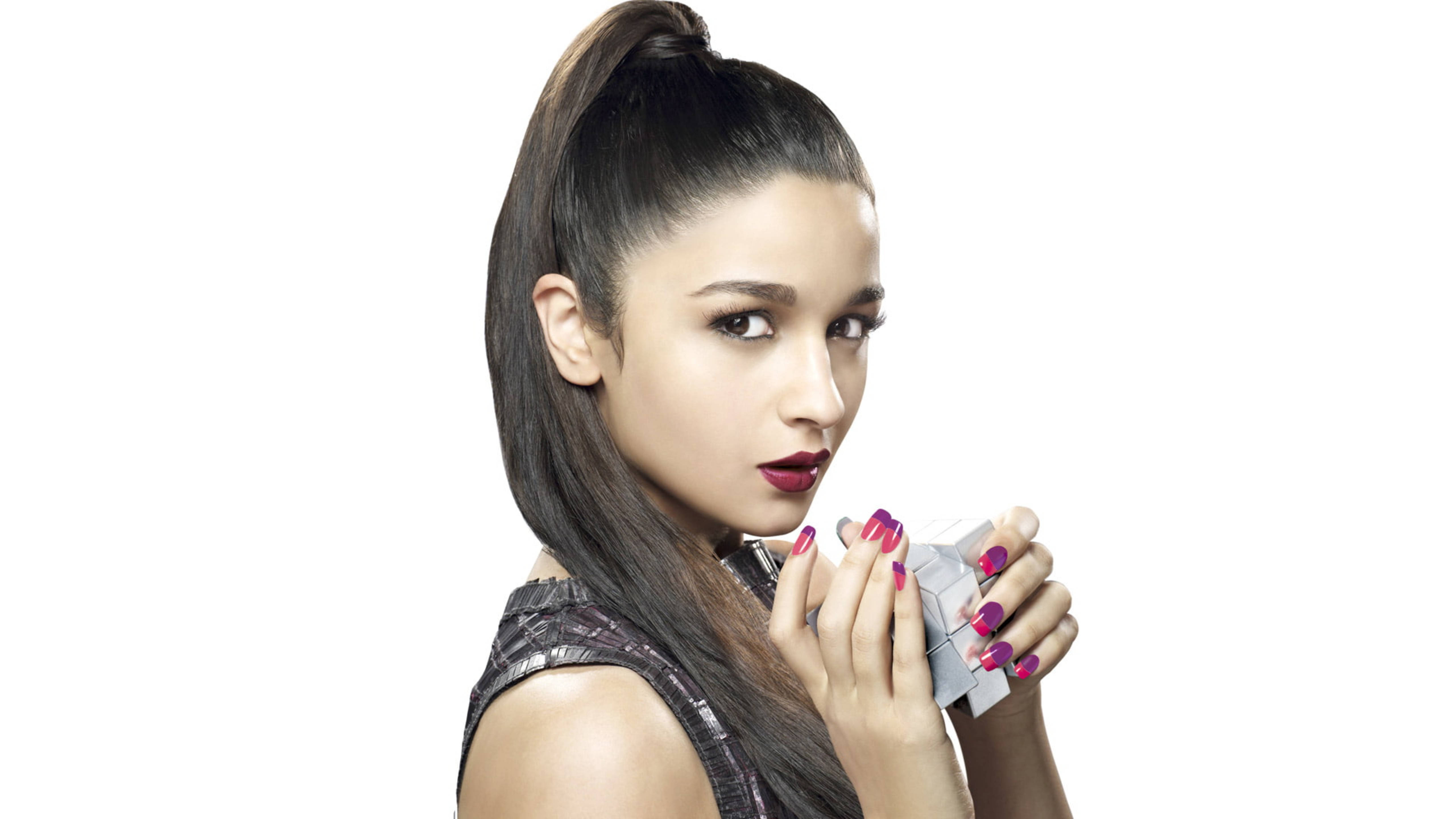 Alia 桌布 壁紙 — 一位深色頭髮高馬尾的女性，在純白背景前拿著一個銀色立方體。
