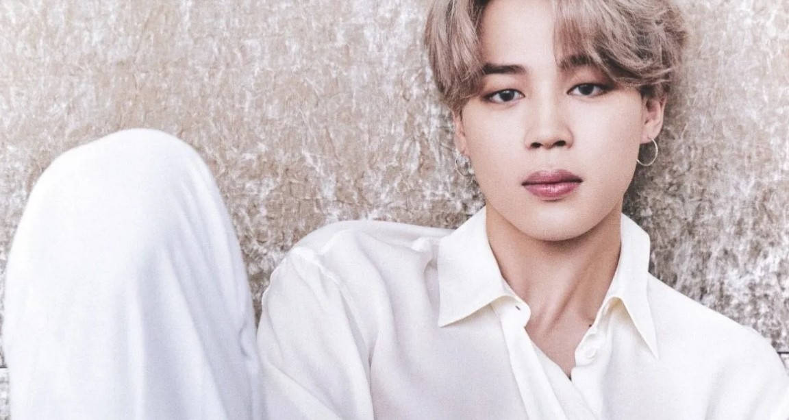 BTS 智旻 桌布 壁紙 — 一位淺棕色頭髮、戴著圓環耳環的年輕男子，穿著白色襯衫，靠著質感米色牆壁放鬆地坐著。