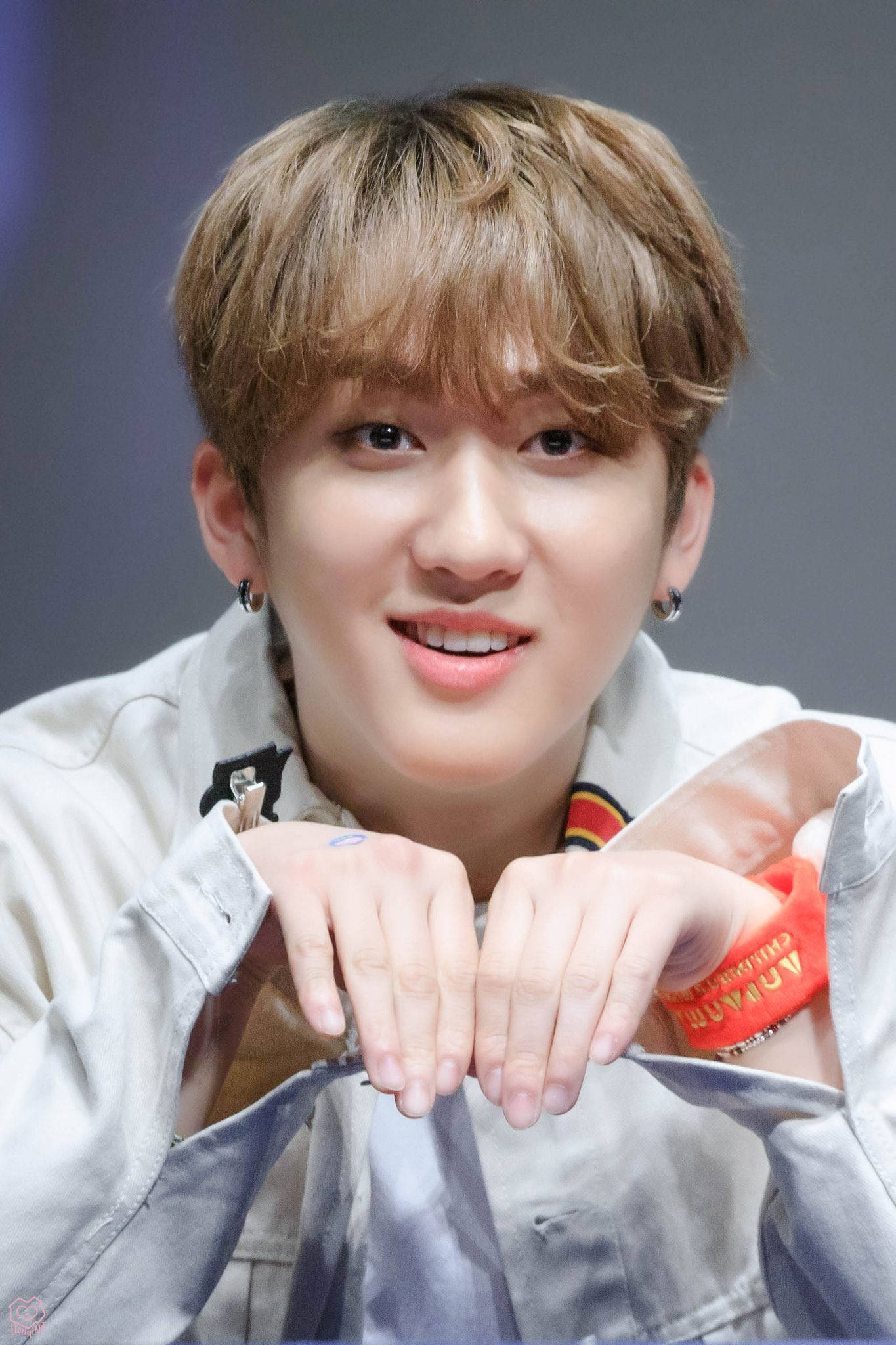 Stray Kids 桌布 壁紙 — 一位淺棕色頭髮、笑容燦爛的年輕男子，雙手比出心形，身穿輕便外套和紅色腕帶。