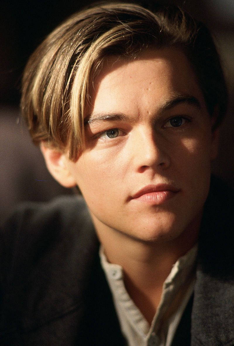 Dicaprio 桌布 壁紙 — 一位淺棕色頭髮、藍色眼睛的年輕男子在溫暖的方向性燈光下若有所思地凝視著鏡頭。