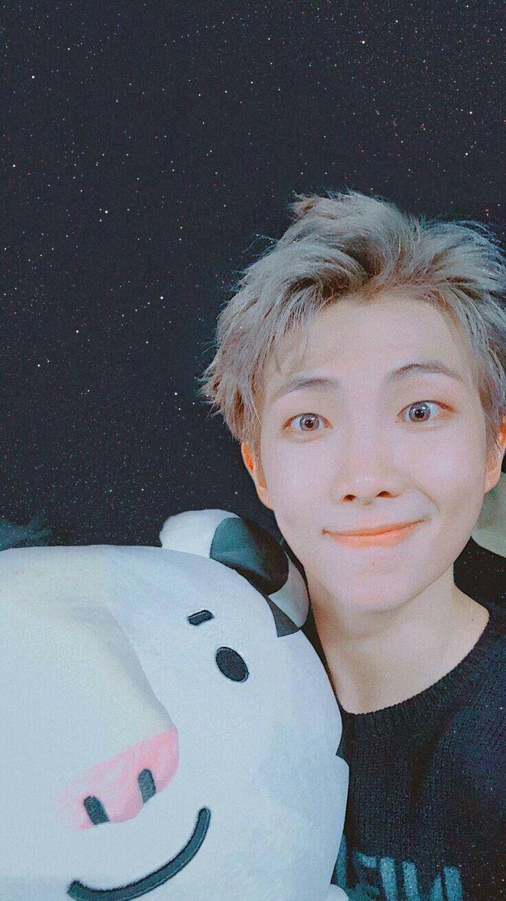 Namjoon 桌布 壁紙 — 一位淺色頭髮的年輕人微笑著，手持白色牛玩偶，背景是星空夜空。